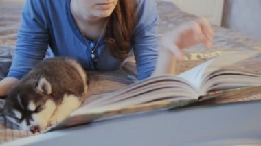 Köpek yavrusu Siberian dış yapraklar ve kız yatakta bir kitapla