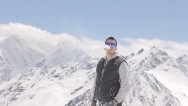 Νεαρός άνδρας που καπνίζει ένα ηλεκτρονικό τσιγάρο σε ένα φόντο από όμορφα βουνά — Αρχείο Βίντεο