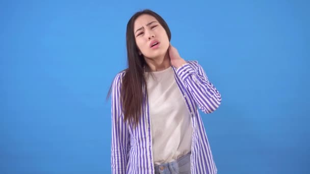 Красивая молодая азиатка с болью в шее, стоящая на синем фоне — стоковое видео