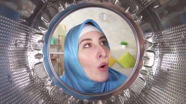 Young muslim woman happily examines the drum of a washing machine — Stock video