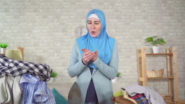 Young muslim woman in a national headscarf is engaged in Ironing and burns her finger — Stock video