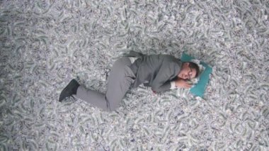 Bir iş adamı, banknotların arka planında bir yastık dikey video ekranında uyur.