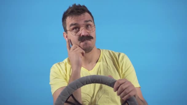 Portré figyelmes férfi szörny bajusszal vezetés egy autó egy kék háttér izolátum — Stock videók