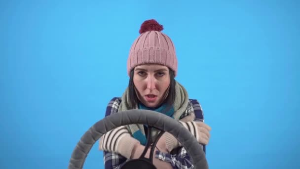 Παγωμένη νεαρή γυναίκα πηγαίνει πίσω από το τιμόνι σε ένα μπλε φόντο απομονωμένη, αργή mo — Αρχείο Βίντεο