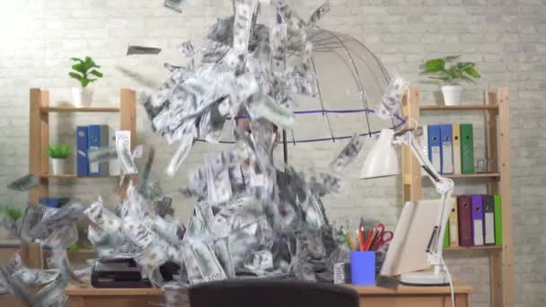 Незвичайний бізнесмен з парасолькою сидить за столом в офісі і повільні банкноти падають на нього, повільний мо — стокове відео
