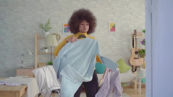 Africká žena s afro účesem se snaží na oblečení před zrcadlem v jeho moderním bytě — Stock video