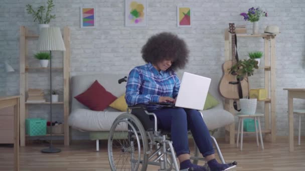 Niepełnosprawna Afroamerykanka z afro fryzurą na wózku inwalidzkim używa laptopa — Wideo stockowe