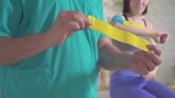 손에 제복을 입은 물리 치료사가 색깔있는 신축성 방추사 테이프를 보여 줍니다. — 비디오