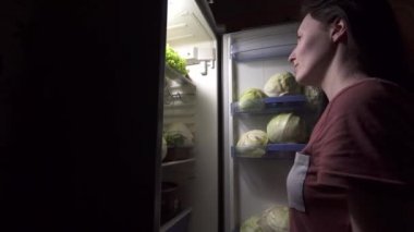 Diyetteki kız salata yemek için buzdolabına bakıyor.