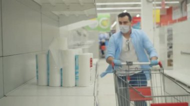 Maske takan ve eldiven takan bir adam panik içinde tuvalet kağıdı alır.