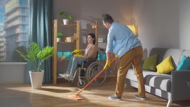 Um par de cônjuges uma jovem mulher com deficiência em uma cadeira de rodas estão limpando a casa — Vídeo de Stock