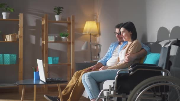 A couple of spouses a young disabled woman in a wheelchair spend time together sitting on the couch close up — Stock Video