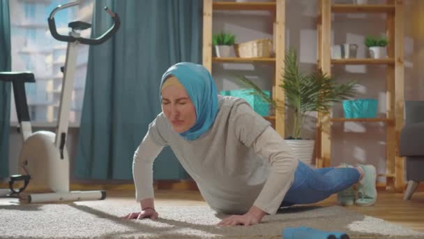 全国のスカーフの若いイスラム教徒の女性は、リビングルームでプッシュアップをしようとします — ストック動画