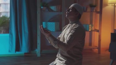 Geleneksel giysiler içinde, evinde dua eden orta yaşlı Müslüman bir adamın portresi.