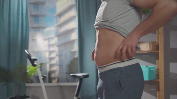El hombre tiene problemas con el sobrepeso mientras está de pie en la sala de estar — Vídeos de Stock