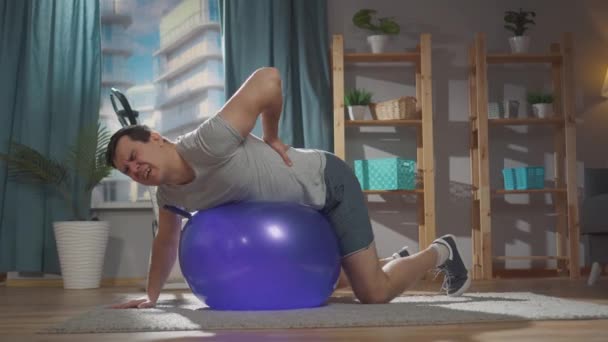 Grave dolore in un uomo durante una lezione di fitness su una palla da ginnastica a casa — Video Stock