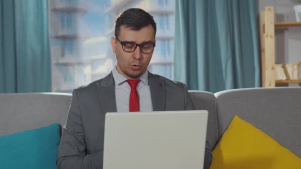 Alvorlig kontorarbejder i jakkesæt og shorts sidder i stuen og taler på en bærbar computer på arbejdspladsen – Stock-video