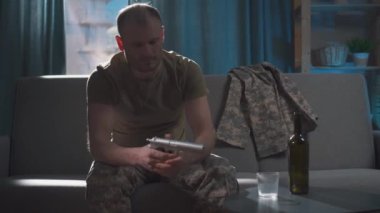 Üniformalı bir asker elinde silahla evde oturur.