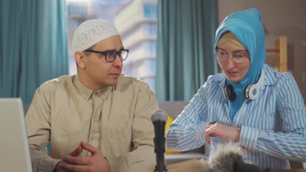 ปิดขึ้นหญิงสาวมุสลิมและชายมุสลิมบันทึกพอดคาสต์การสัมภาษณ์ในขณะที่นั่งอยู่หน้าไมโครโฟนในห้องนั่งเล่น — วีดีโอสต็อก
