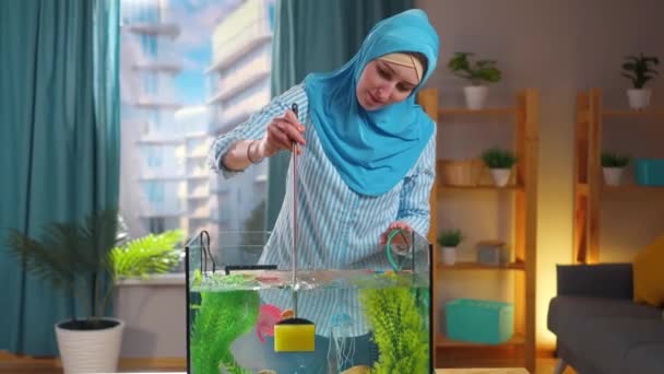 Mulher muçulmana em lenço de cabeça nacional limpa aquário com esponja — Vídeo de Stock