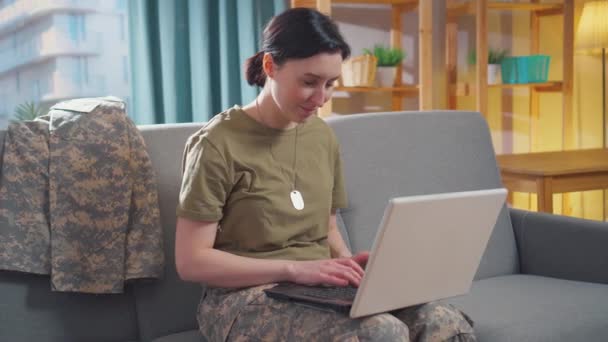 Молодая улыбающаяся военная женщина сидит за своим ноутбуком — стоковое видео