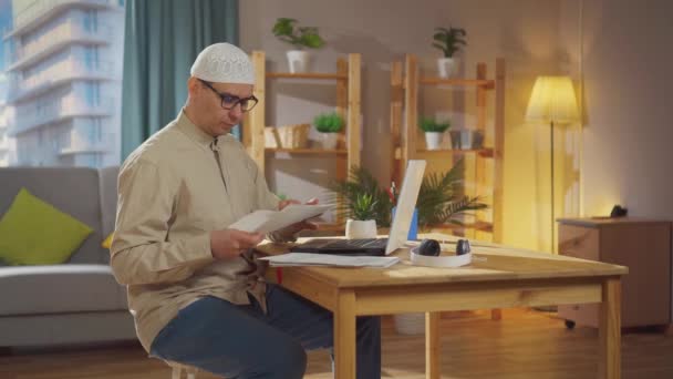 Kafatası şapkalı Müslüman bir adam evde dizüstü bilgisayarla çalışıyor. — Stok video