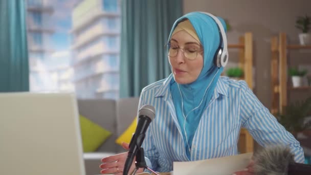 Portrait young muslim woman records a podcast while sitting in front of a microphone in her living room — Stock Video