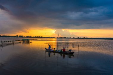 Long An, Vietnam - 22 Ağustos 2024: güzel, huzurlu bir gün batımı. Yerel bir aile, bir baba, bir çocuk ve bir anne küçük ahşap bir teknede ağlarıyla ilgilenirken ya da güneş ufkun altına batarken balık tutarken görülürler.