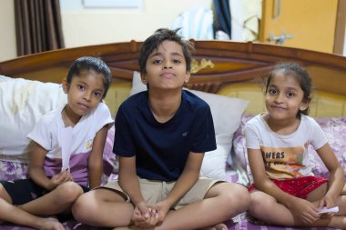 Oturma odasındaki bir yatakta üç çocuk oturuyor. Bir oyun oynarken gülümsüyorlar ve birbirleriyle etkileşime geçiyorlar..