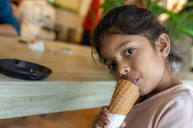 Bir çocuk öğleden sonra bir kafede bir masada otururken dondurma külahının keyfini çıkarır..