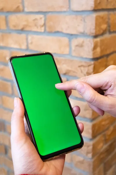 Tuğla duvar arkasında boş ekranlı akıllı telefon tutan kadın..