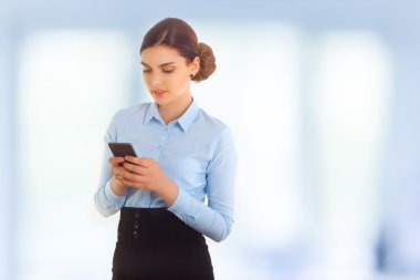 Smartphone üzerinde mavi arka plan kullanarak iş kadını. Mavi tişört giyiyor. Babette saç modeli.