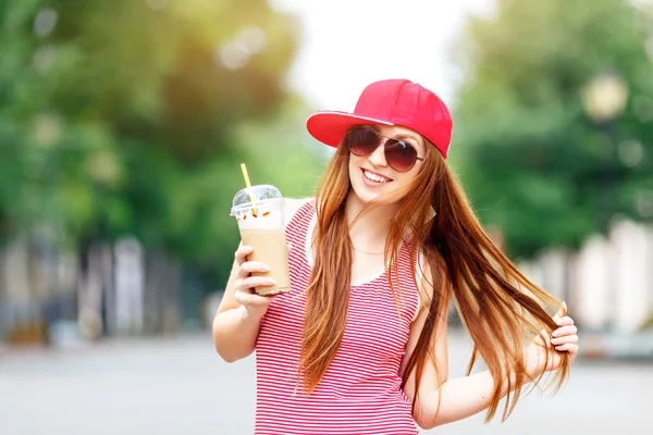 Moda şehir portresi şık hipster milkshake, kırmızı çizgili kadınla elbise, kırmızı bere ve spor ayakkabı, makyaj, uzun esmer saçlar, yalnız hafta sonu yürüyüş zevk tatil Avrupa'da, modern trendy