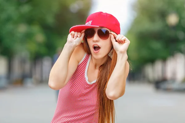 在欧洲，现代新潮时尚城市肖像的时尚时髦的女人，红色条纹身穿红色帽和运动鞋，化妆，太阳镜，长黑发毛，独自行走在周末，享受假期 — 图库照片