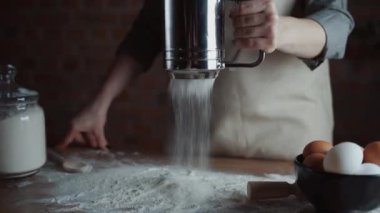 Kadın fırın şefi masayı süzgeçten un ayıklayarak ev yapımı ekmek yapmaya hazırlanıyor..