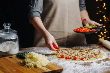 Ev yapımı pizza pişirme. Kadın el aşçısı hamura domates dilimi döküyor. Salgın nedeniyle karantina altında gıda hazırlama kavramı.