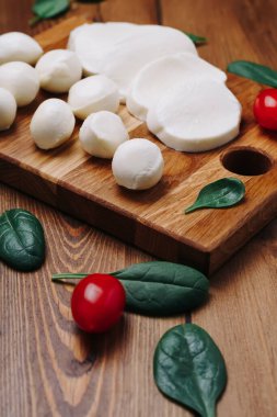 Beyaz küçük mozzarella peynir topları, tahtanın üzerinde ıspanak yaprakları ve domatesler.