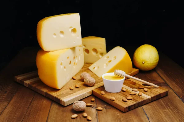 Ost på bordet, mörk bakgrund. Medium hård ost huvud edam, gouda, parmesan med burk honung på trä skärbrädor. Hälsosam kost koncept. Stockbild