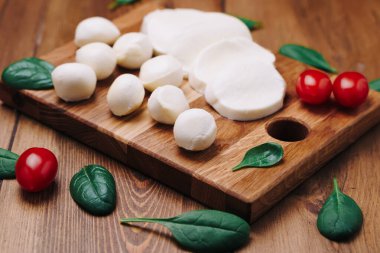 Beyaz küçük mozzarella peynir topları, tahtanın üzerinde ıspanak yaprakları ve domatesler.