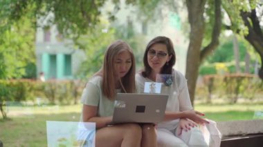 Sosyal ağ hizmeti kavramı. Genç bir kadın, emekli annesine laptopuyla parkta otururken yardım ediyor. İletişim ağı. Hologram yüzen fotoğraflar.