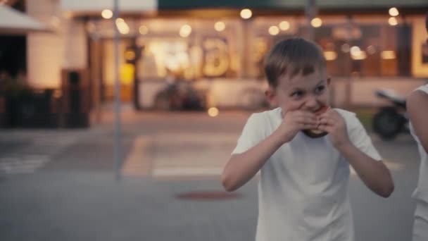 Két éhes fiatal fiú hamburgert eszik az esti utcában. Csúszás 4K lövés