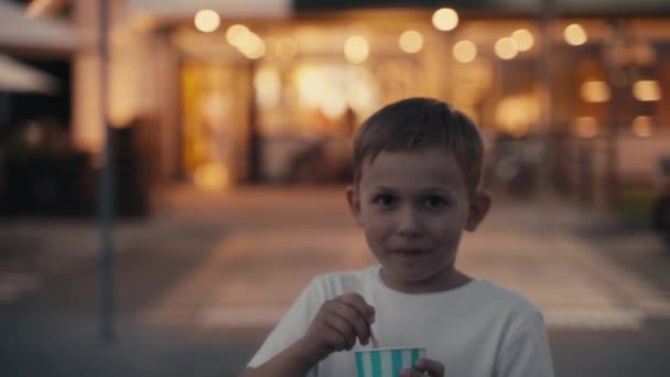 Pequeño niño hambriento comiendo helado en la calle de la noche. — Vídeos de Stock