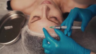 Güzellik ve enjeksiyon konsepti. Bir kadının alnına iğne yapan bir güzellik uzmanının yakın çekimi..