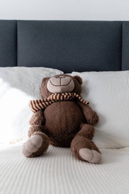 Çocukluk Konforu: Yumuşak pelüş bir oyuncak ayı Sunlit yatak odasında Buruşuk beyaz yatakta dinleniyor