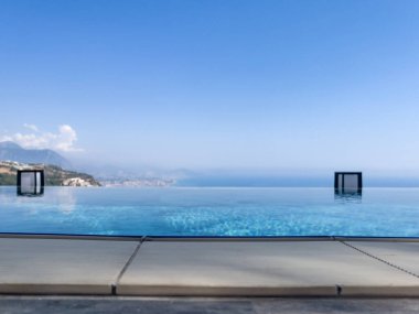 Lüks Resort Görünümü: Krom Şelale Özellikli Mavi Sonsuzluk Kenar Havuzu ve Panoramik Şehir Çerçeveli Palmiye Ağacı ve Okyanus Ufku