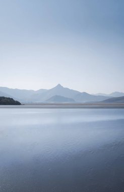 a vertical shot of a lake with a beautiful blue sky in the background