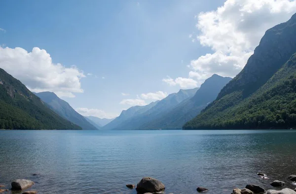 a beautiful scenery of a lake surrounded by mountains under the cloudy sky in daytime