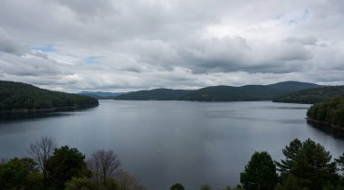 a beautiful shot of a lake surrounded by mountains under the cloudy sky in the forest