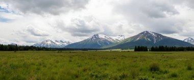 scenic view of mountains and field on cloudy sky background
