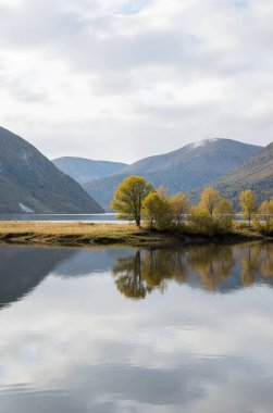 Gökyüzünün altında dağlarla çevrili bir gölün dikey görüntüsü.